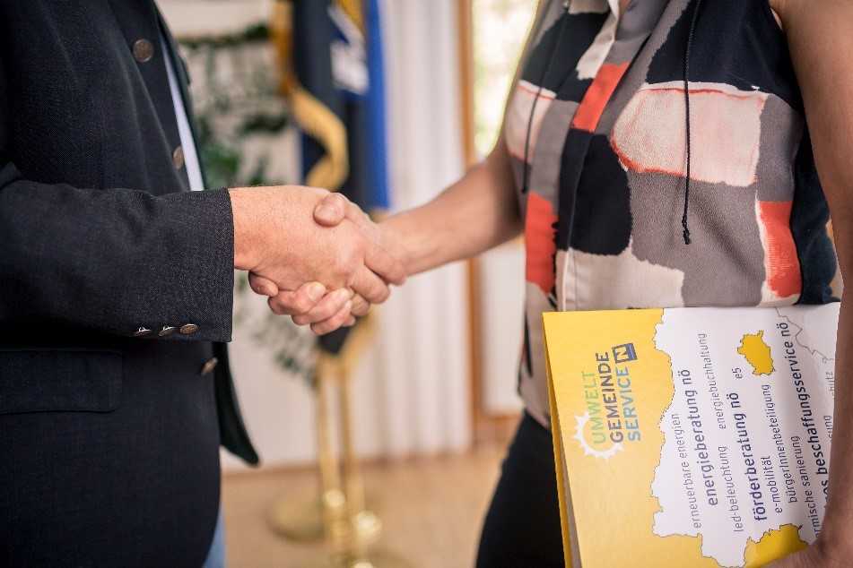 Das Foto zeigt eine Frau udn einen Mann, die sich die Hände reichen. Die Frau trägt in einem Arm eine Mappe des Umwelt Gemeinde Services.