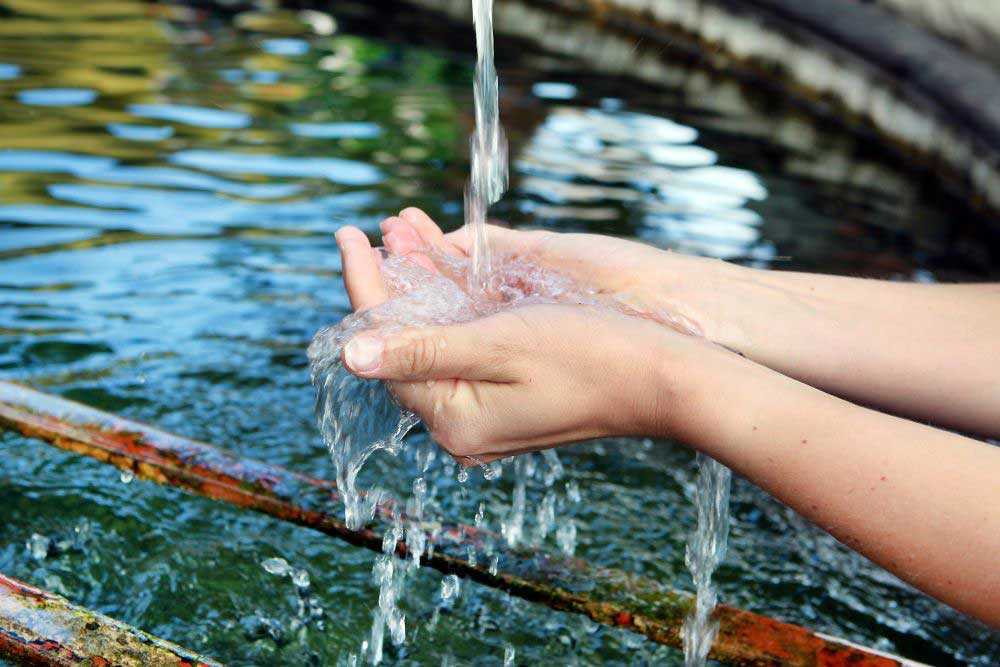 Das Foto zeigt zwei Hände zusammengehalten, um einen Wasserstrahl von oben aufzufangen.